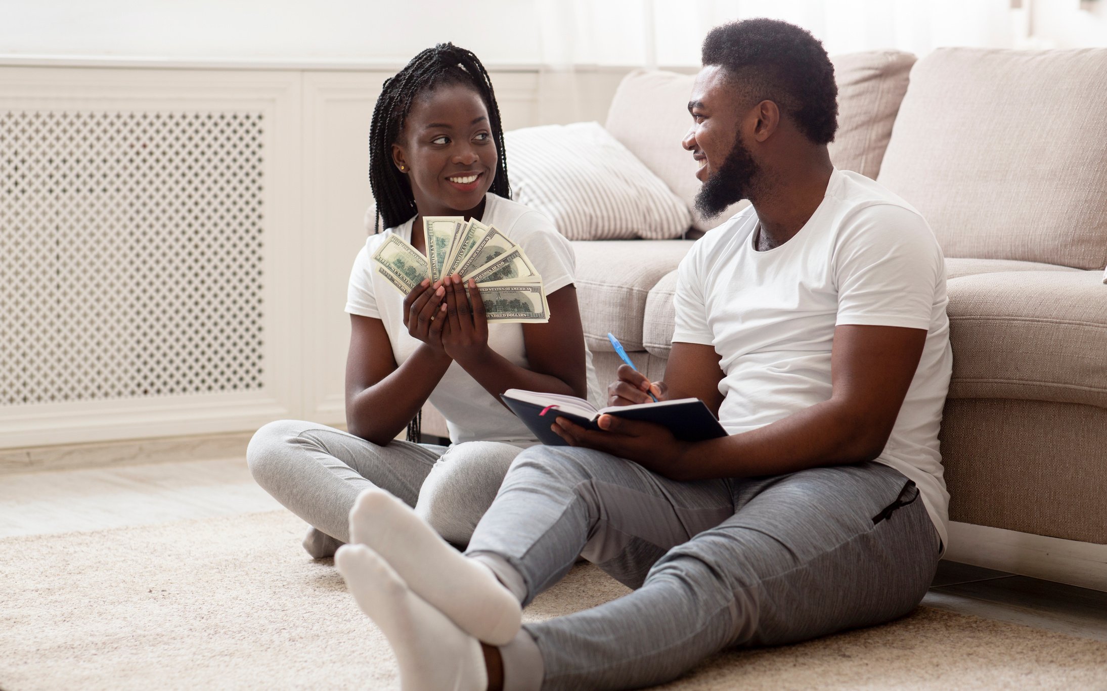 Happy black couple with money and notepad, planning family budget together